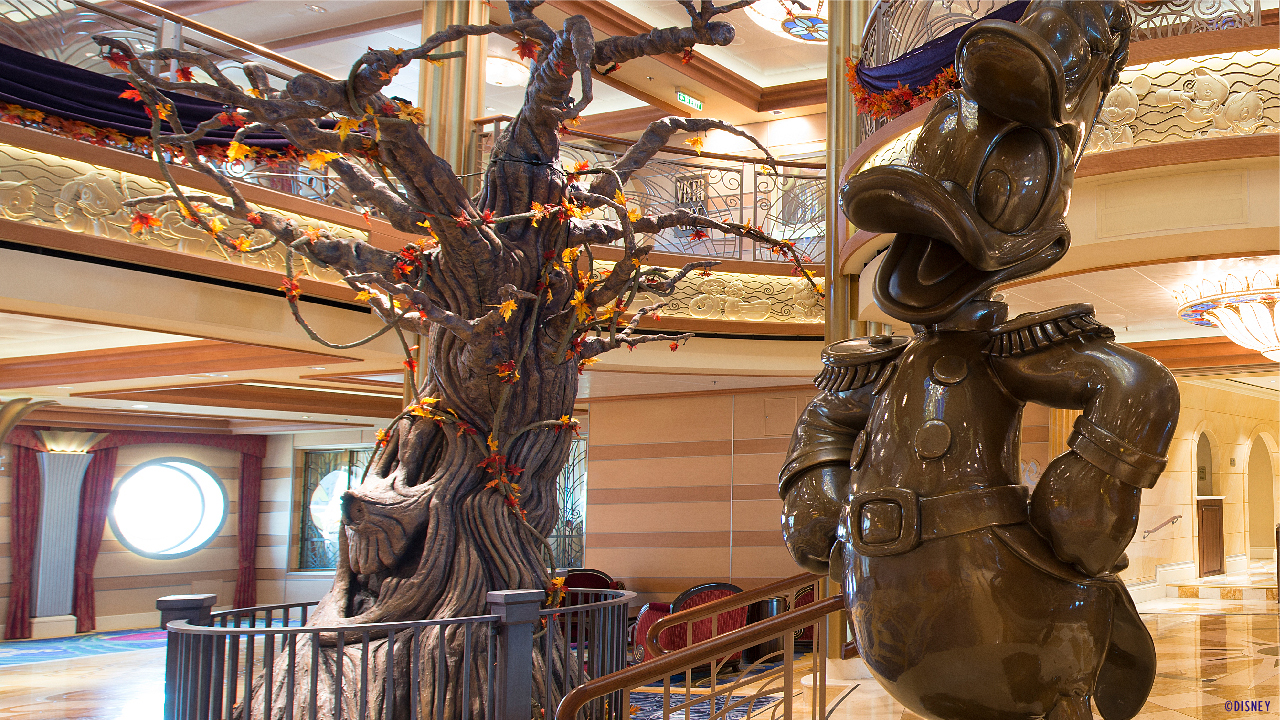 Atrio decorado para Halloween on the High Seas Atrio de Disney Cruise Line con estatua de Donald y decoración del Pumpkin Tree para Halloween on the High Seas